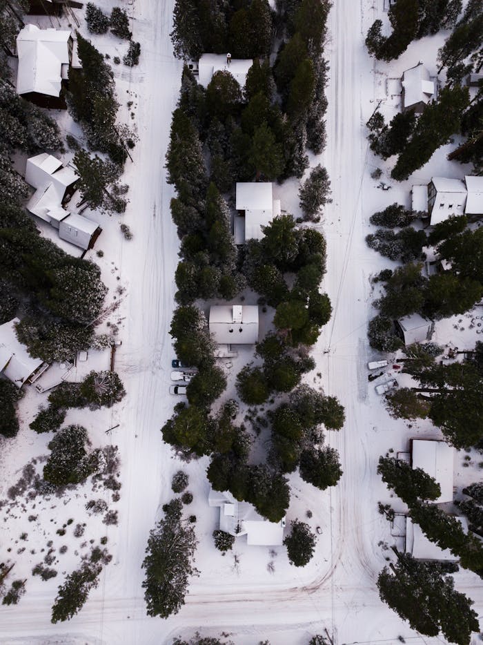 Aerial shot of a snow-covered neighborhood surrounded by trees during winter.